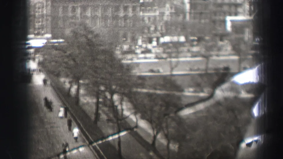 1952 Edinburgh home-movie frame from above, showing a tree-lined street with pedestrians and traffic partly obscured by dark vertical foreground shapes.