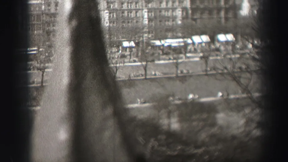 Black-and-white 8mm frame of Edinburgh from above, with pedestrians and vehicles along a tree-lined street framed by dark vertical foreground edges.