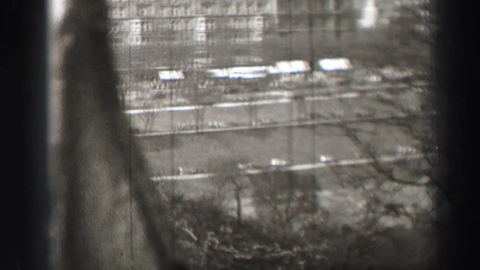 1952 Edinburgh street scene from an elevated viewpoint, with bare trees, road lanes, distant buildings, and partial dark frame obstruction.