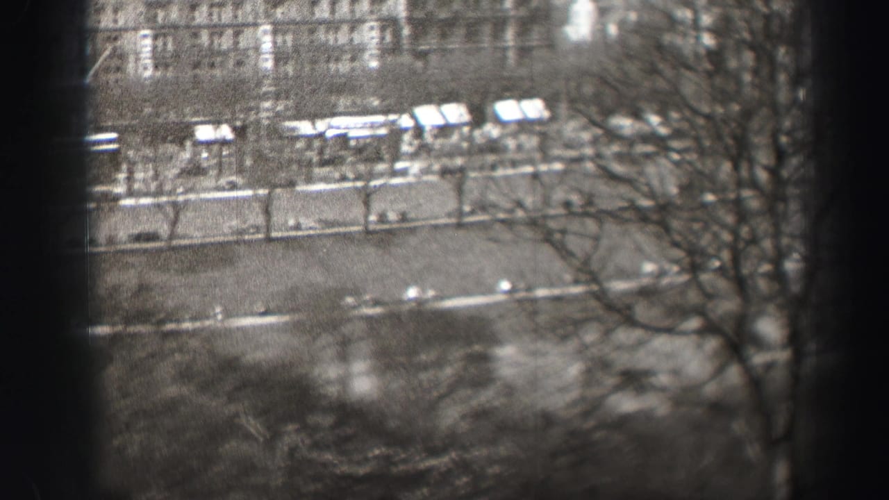 Elevated black-and-white view of an Edinburgh street, with bare roadside trees, light vehicles, sidewalks, and building facades in the distance.