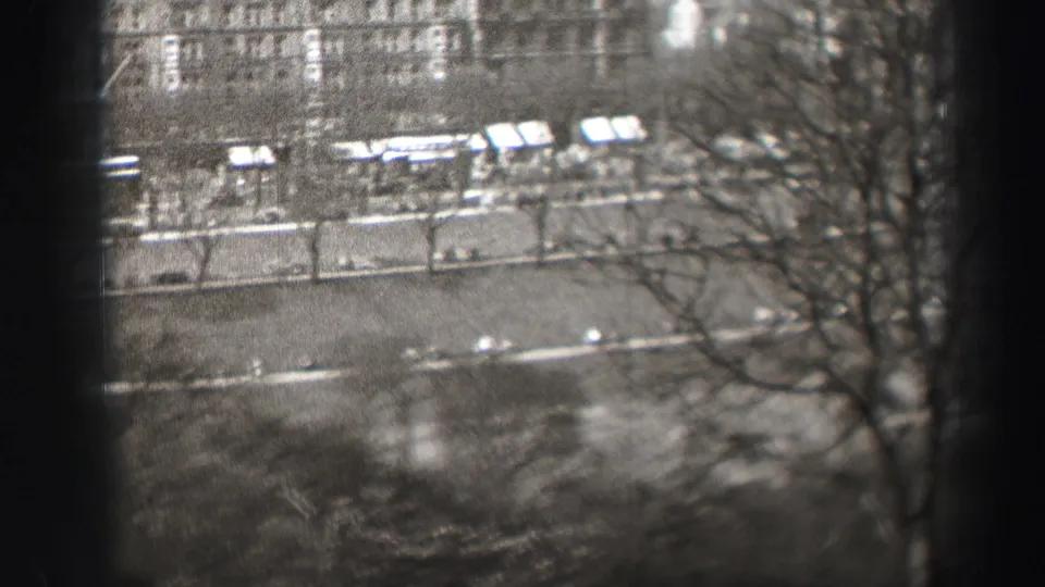 Elevated black-and-white view of an Edinburgh street, with bare roadside trees, light vehicles, sidewalks, and building facades in the distance.