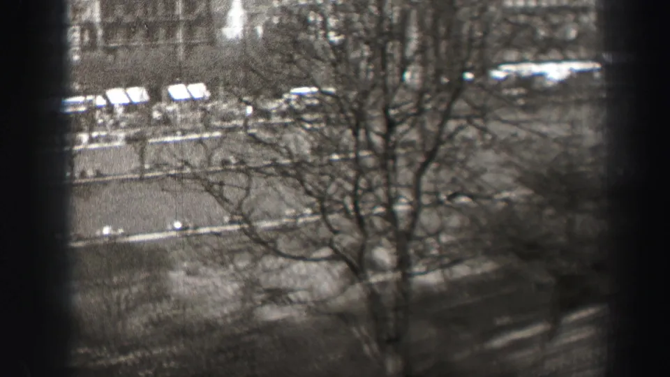 Black-and-white 8mm frame of an Edinburgh street, showing bare trees, small pedestrians, vehicles, and a central dark obstruction from the filming angle.