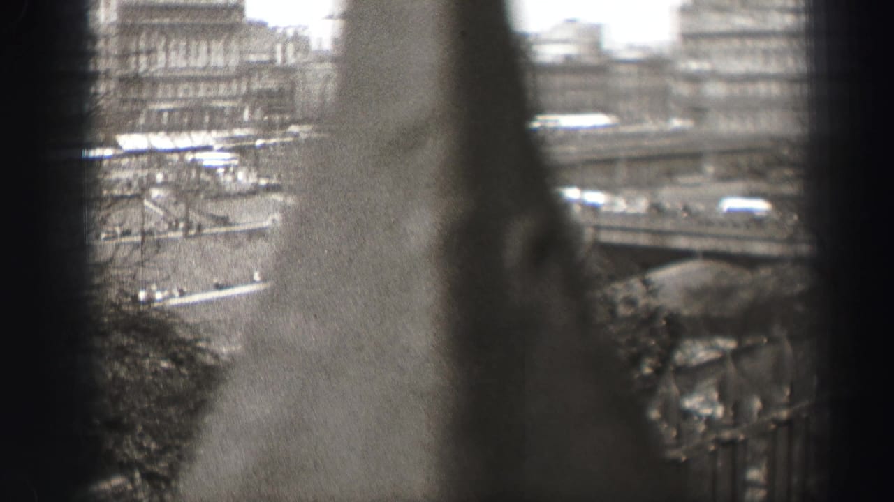 1952 8mm home-movie frame looking through dark window divisions toward Edinburgh streets and distant urban buildings.