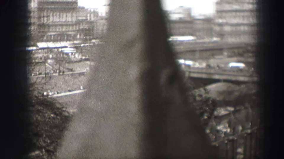 1952 8mm home-movie frame looking through dark window divisions toward Edinburgh streets and distant urban buildings.