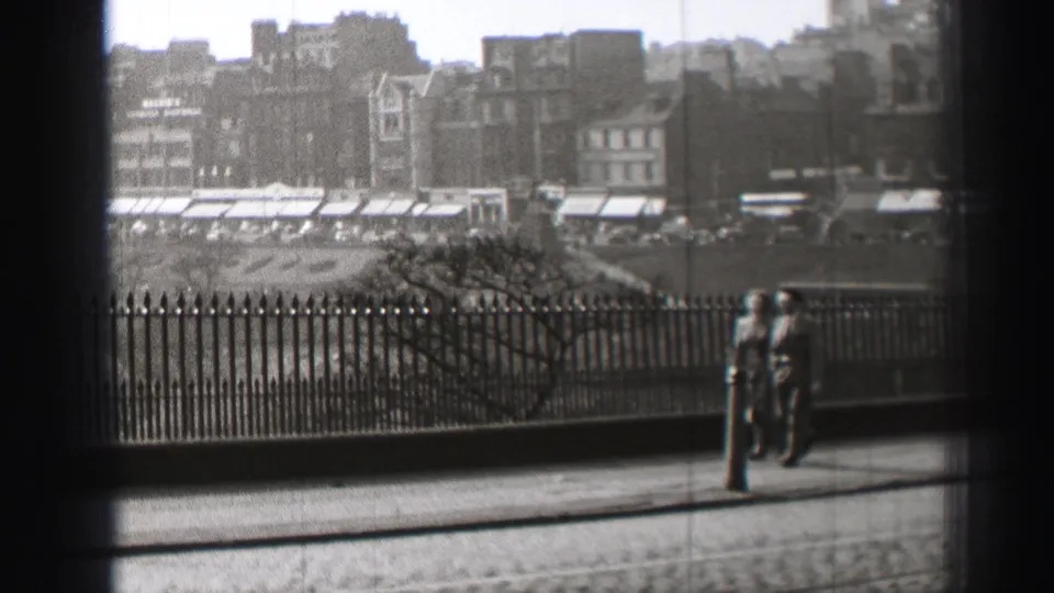 1952 Edinburgh street view with pedestrians near iron railings, tram tracks, and distant urban buildings.