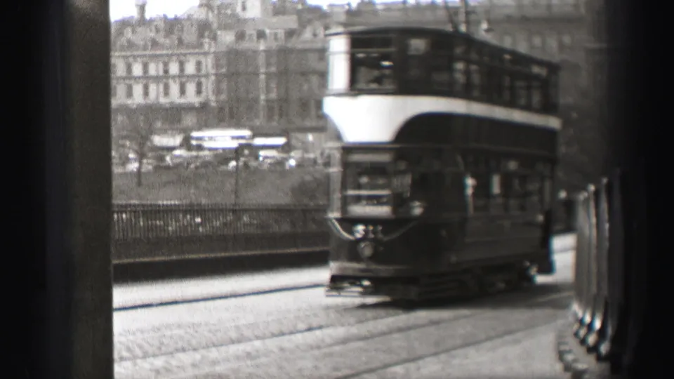 Black-and-white view of a double-decker tram passing through 1952 Edinburgh with urban buildings beyond.