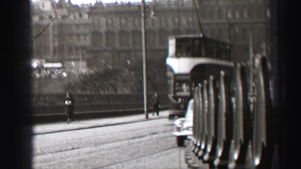 1952 Edinburgh street view with a double-decker trolley, pedestrians, older cars, and large stone buildings seen through a dark foreground barrier.