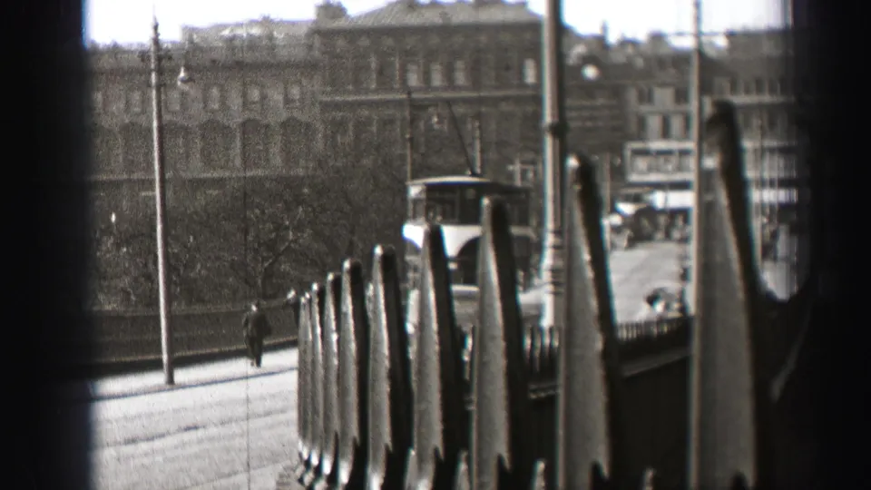 The trolley continues away on a 1952 Edinburgh street, framed by a dark barrier with pedestrians, railings, and city buildings visible.