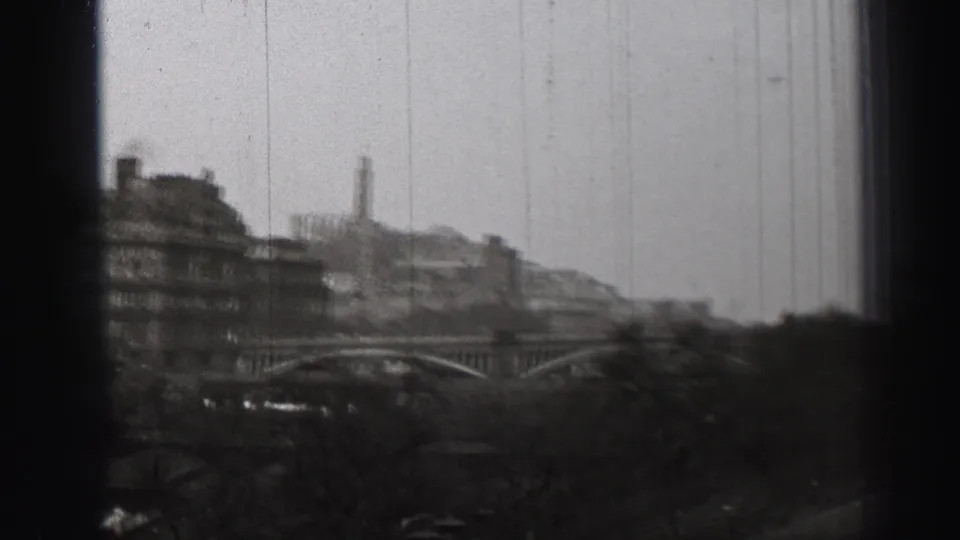 1952 Edinburgh cityscape with distant bridge arches, layered buildings, trees, and a tall vertical structure under a pale sky.