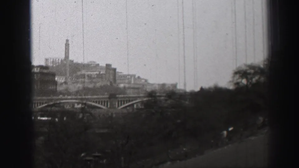 1952 Edinburgh home-movie view of bridge spans, tree cover, distant buildings, and dark window framing at the edge of the shot.