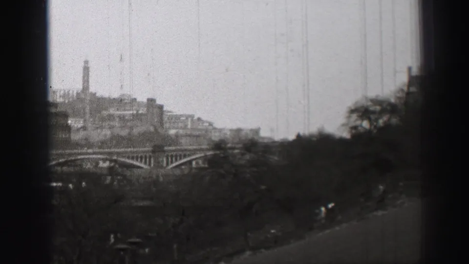 1952 Edinburgh cityscape seen from an elevated viewpoint, with an arched bridge, trees, and dark film-edge obstruction.