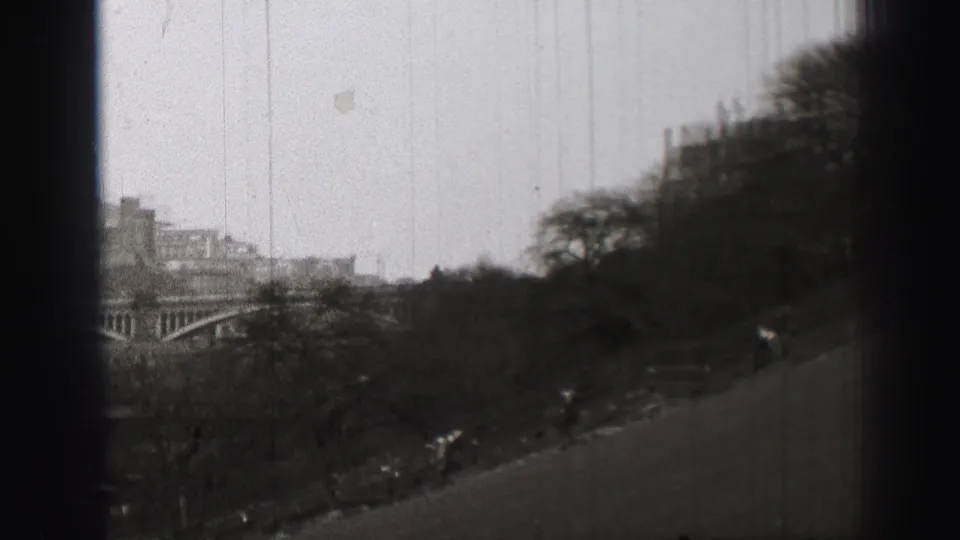 Elevated 1952 Edinburgh view across a sloped park toward an arched bridge and dense city buildings in soft focus.