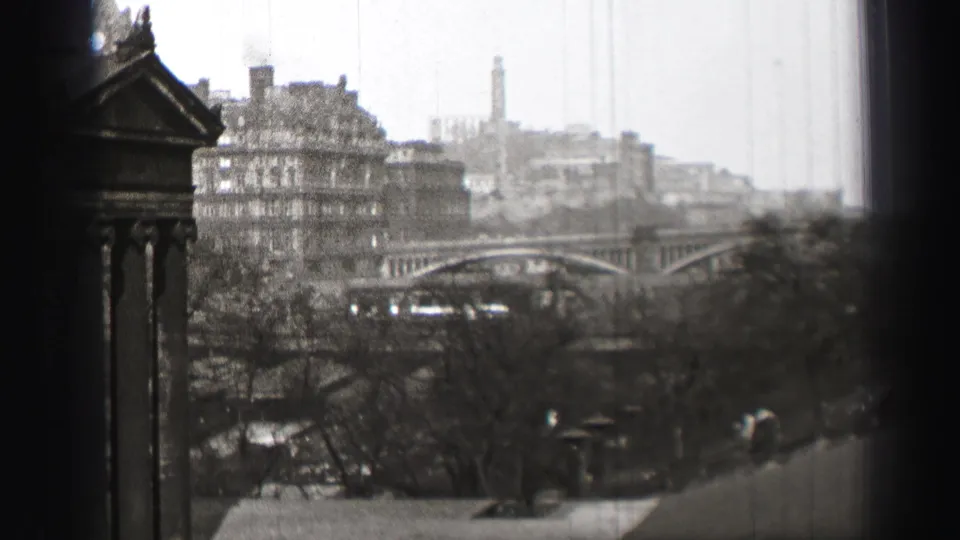 Black-and-white 1952 Edinburgh frame showing a columned structure at left and the bridge, buildings, trees, and distant tower beyond.