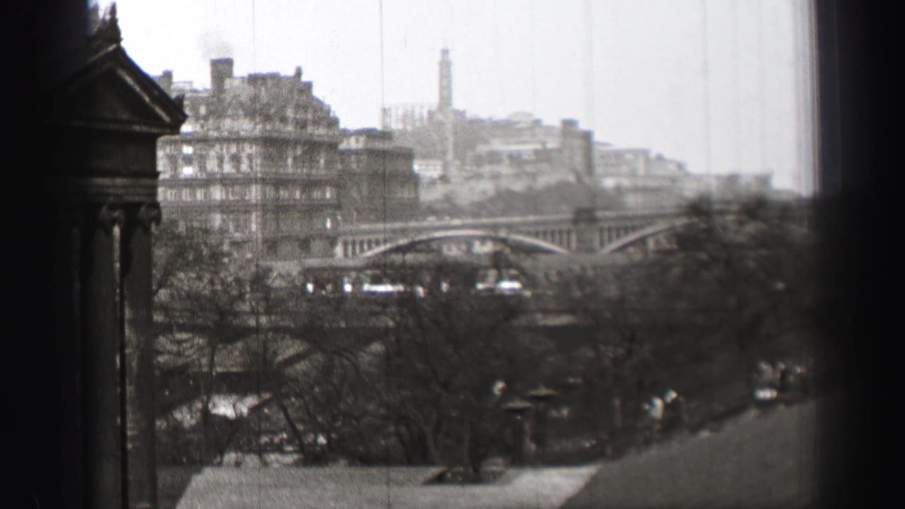 1952 Edinburgh home-movie frame showing an elevated city view with an arched bridge, stone buildings, leafless trees, and a dark edge obstruction.