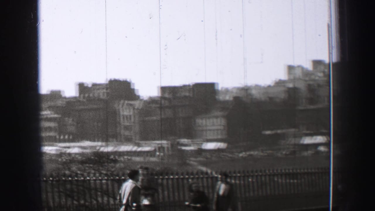 City buildings behind a railing with pedestrians in the foreground and a dark vertical obstruction near center.
