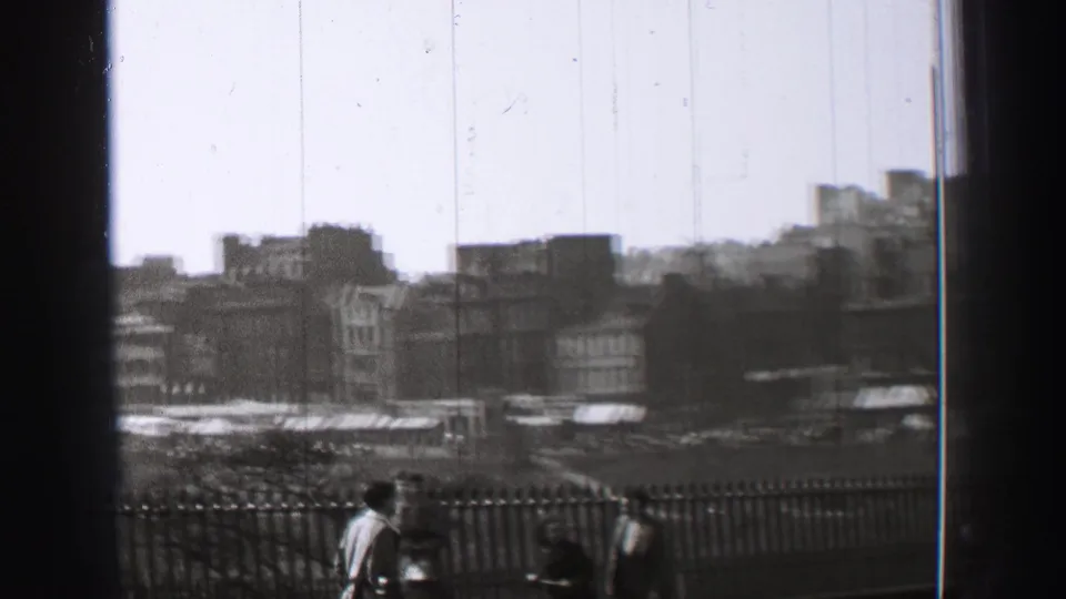 1952 Edinburgh street-level overlook with pedestrians by a railing, distant buildings, possible traffic, and black-and-white film wear.