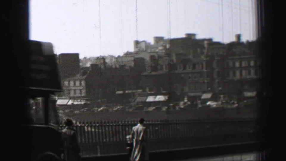 1952 Edinburgh home-movie view of a person by a railing, with multi-story buildings, vehicles, and a dark obstruction at the frame edge.