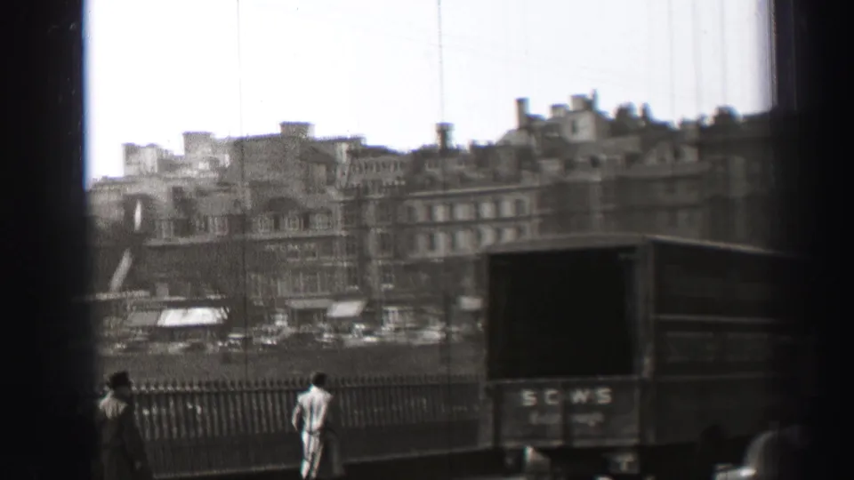 1952 Edinburgh bridge view with pedestrians by the railing, a marked delivery truck, overhead wires, and stone buildings in the distance.