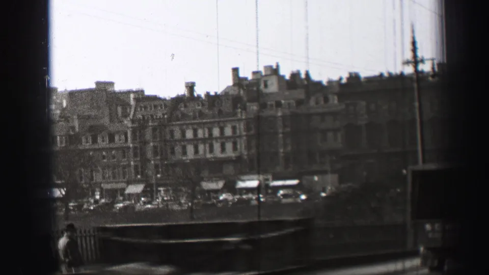 1952 Edinburgh city street view with bridge railing, distant stone facades, parked cars, a pedestrian, and visible film edge shadow.