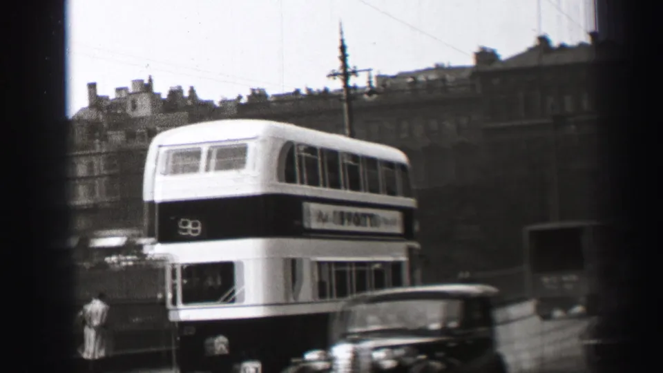 1952 Edinburgh street view with a route 9 double-decker bus, vintage cars, pedestrians, and overhead wires seen through a dark frame.