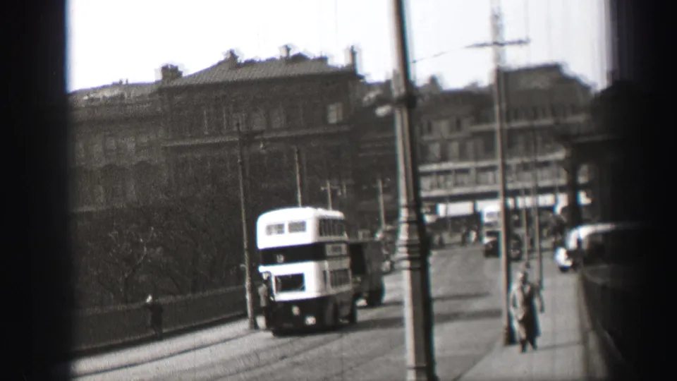 1952 Edinburgh street scene with the bus moving away, pedestrians on the pavement, overhead wires, and multi-story buildings beyond.