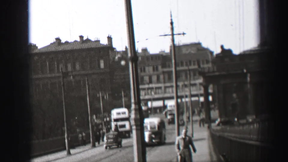 Soft 1952 Edinburgh street frame showing bus traffic, pedestrians, road poles, railings and a handheld home-movie view.
