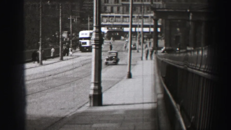1952 Edinburgh road scene with a double-decker bus in the distance, a car, pedestrians, poles and bridge-like railings.