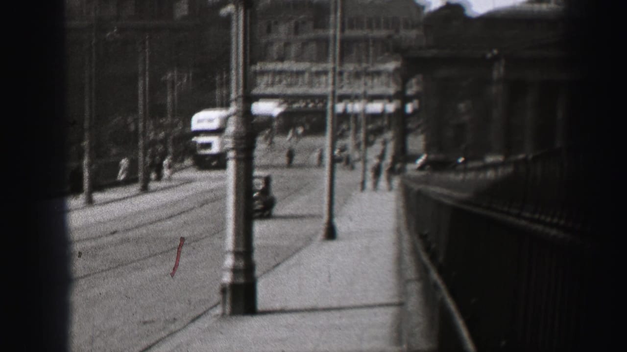1952 Edinburgh street view with pedestrians, lampposts, railings, road traffic, and stone buildings in soft 8mm focus.