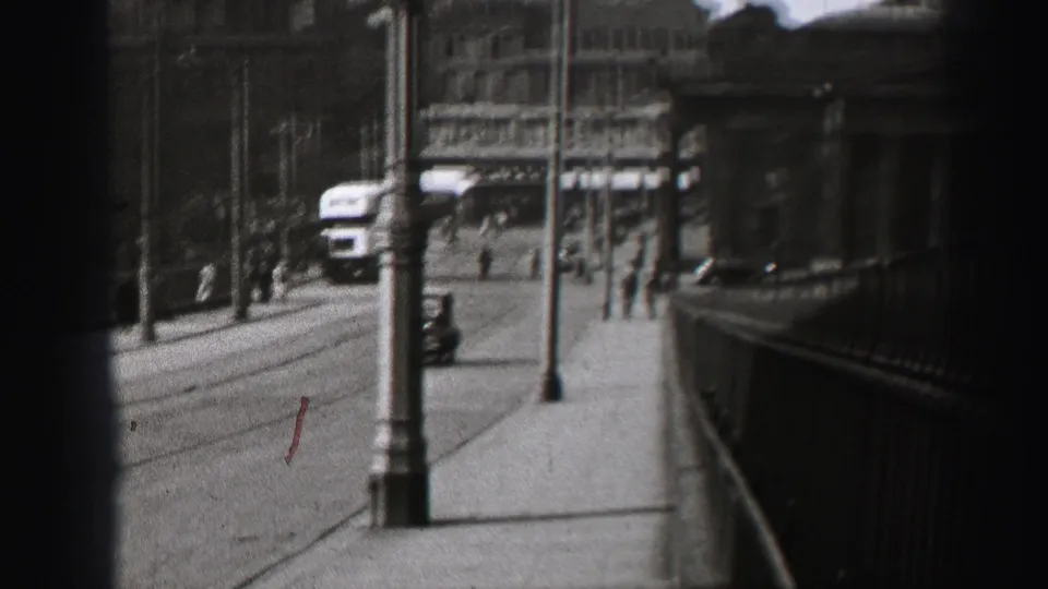 1952 Edinburgh street view with pedestrians, lampposts, railings, road traffic, and stone buildings in soft 8mm focus.