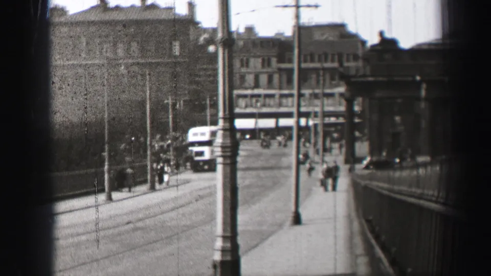 1952 Edinburgh urban street frame with pedestrians, a double-decker bus, lampposts, railings, and stone facades.