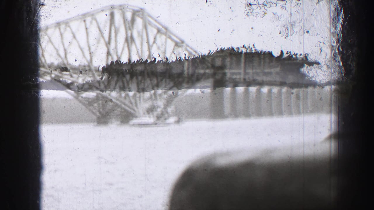 1952 8mm view of the Forth Bridge across the Firth of Forth, partly obscured by dark boat or window framing.