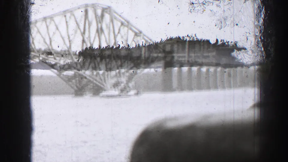 1952 8mm view of the Forth Bridge across the Firth of Forth, partly obscured by dark boat or window framing.