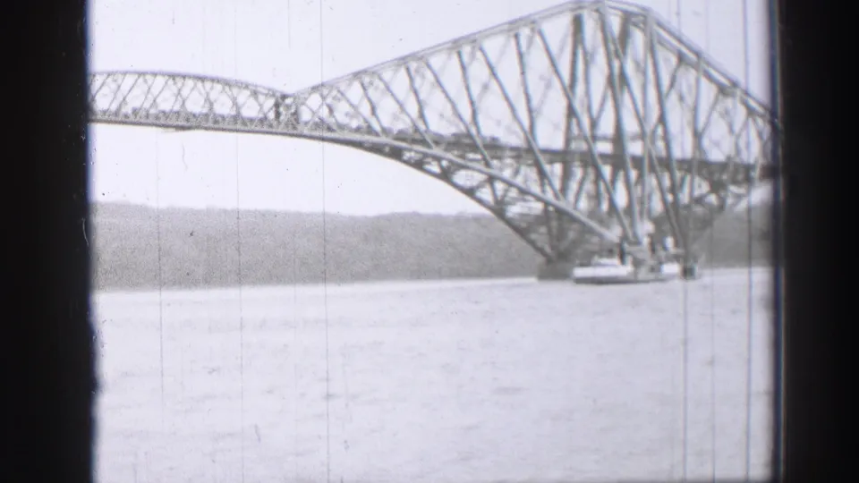 Black-and-white 8mm frame showing the Forth Bridge spanning the Firth of Forth near Edinburgh, viewed from a moving vessel.