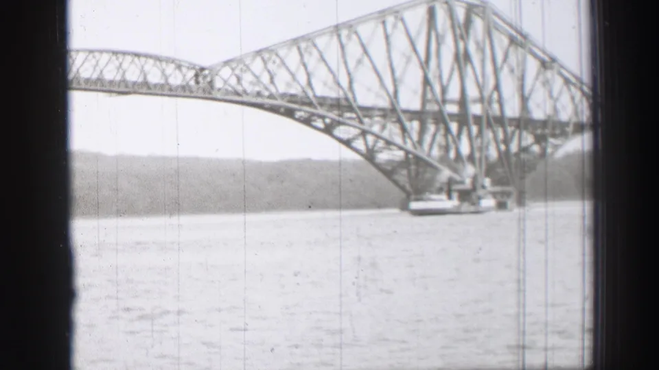 Home-movie frame of the Forth Bridge from the water, with the steel span cropped by dark foreground edges.
