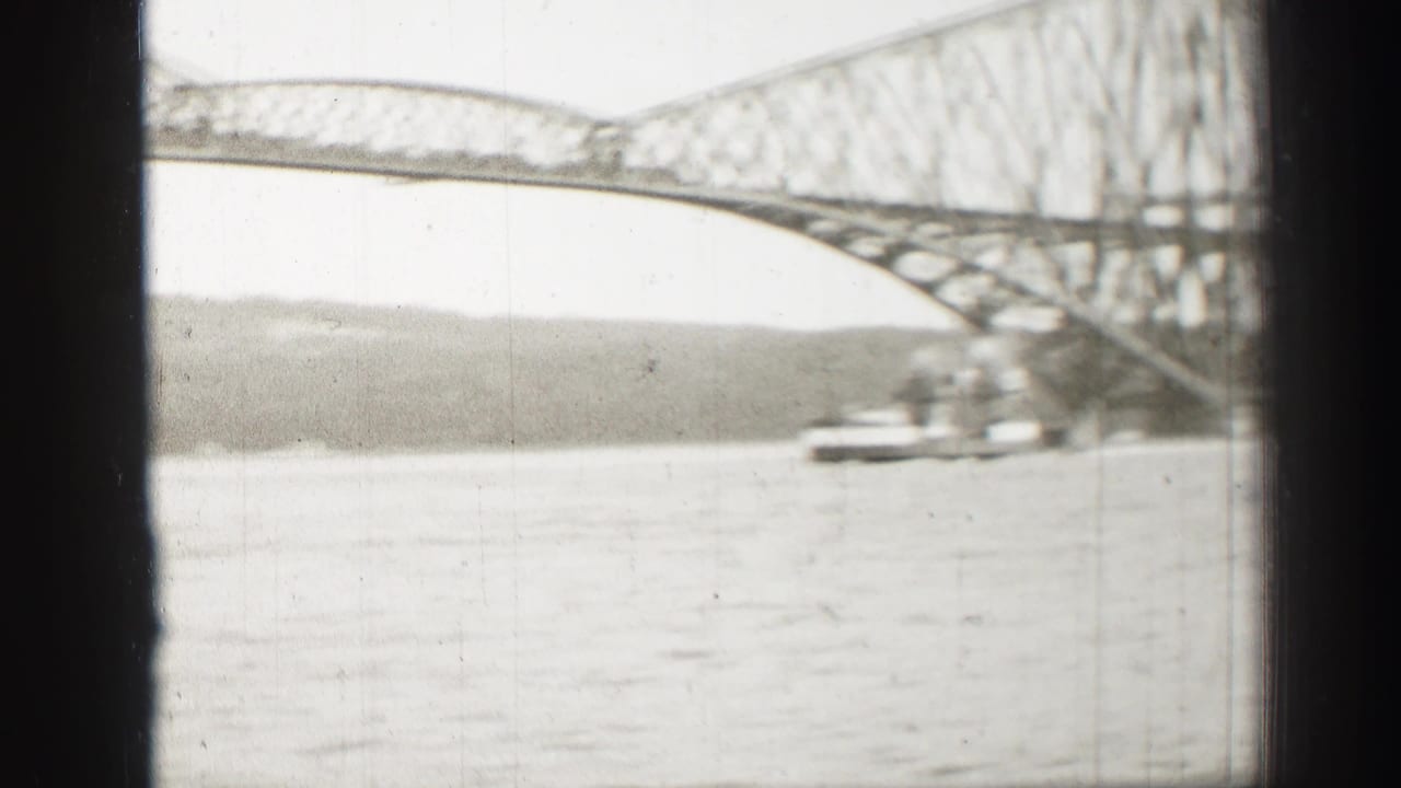 Soft 8mm frame of a steel truss bridge over water in Scotland, with a vessel moving below the span and shoreline beyond.