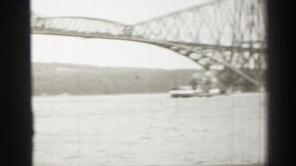 Soft 8mm frame of a steel truss bridge over water in Scotland, with a vessel moving below the span and shoreline beyond.