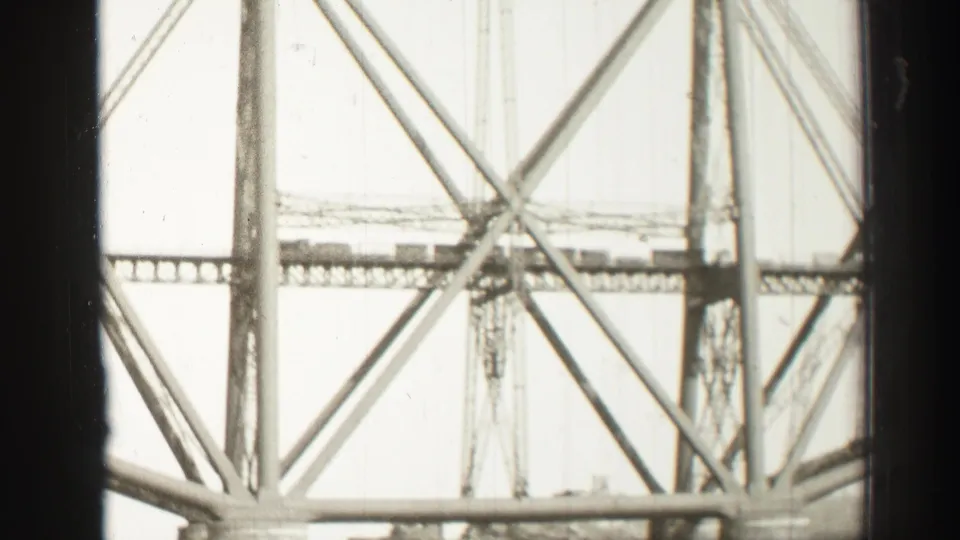 Monochrome 8mm frame from Scotland showing close bridge cross bracing, vertical supports, and the lower span over water.