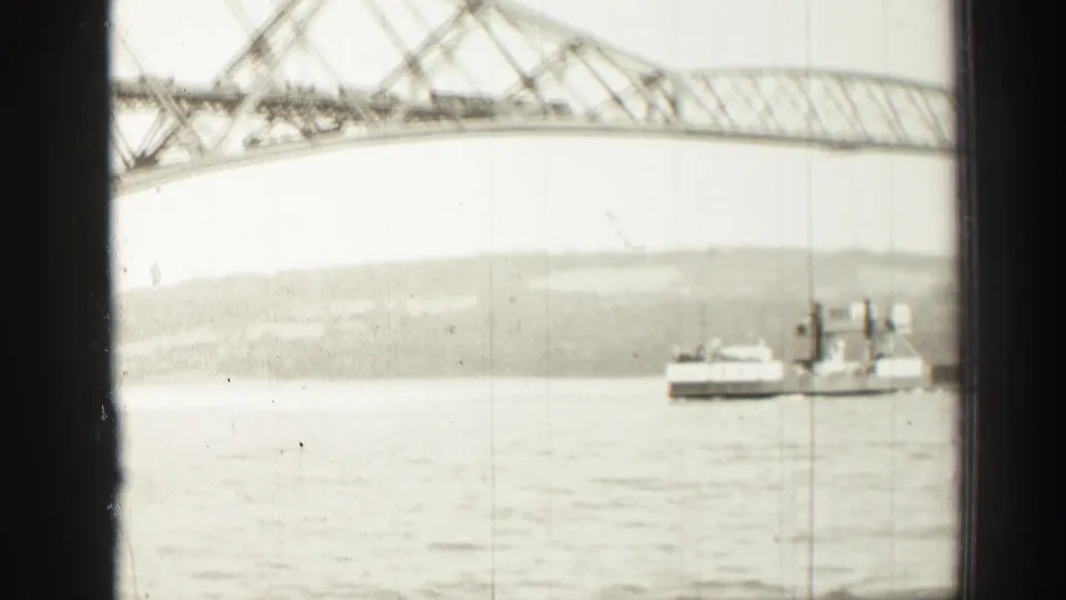 1952 Edinburgh-area 8mm frame showing a ferry or workboat on water beneath a steel truss bridge, seen through dark frame edges.