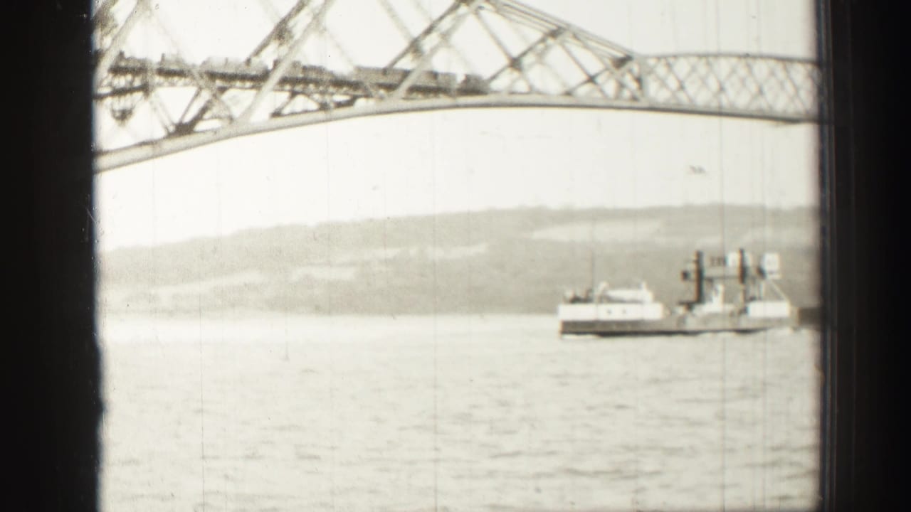 Soft 8mm view of a ferry or work vessel beneath a steel bridge span near Edinburgh, with shoreline hills in the distance.