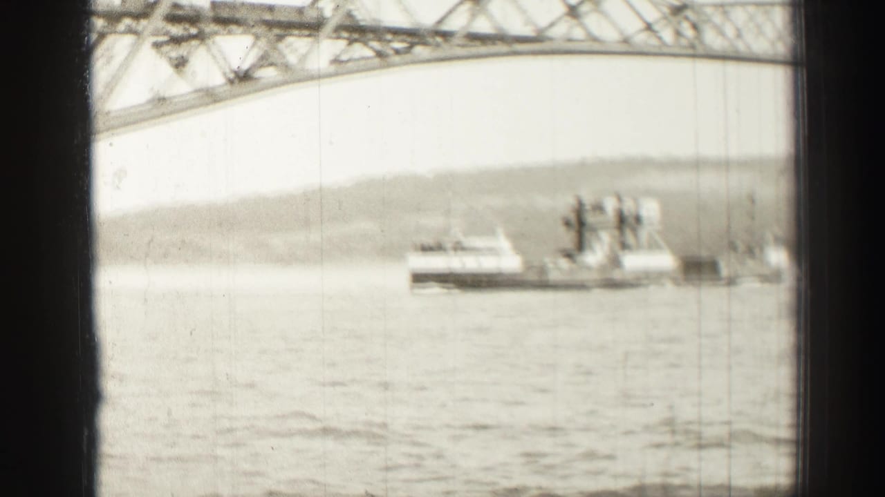Ferry boat crossing a wide river beneath the upper span of a steel bridge.