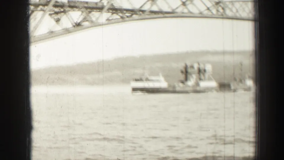 1952 8mm home-movie frame of a ferry moving across water below a large steel bridge in Edinburgh, Scotland.