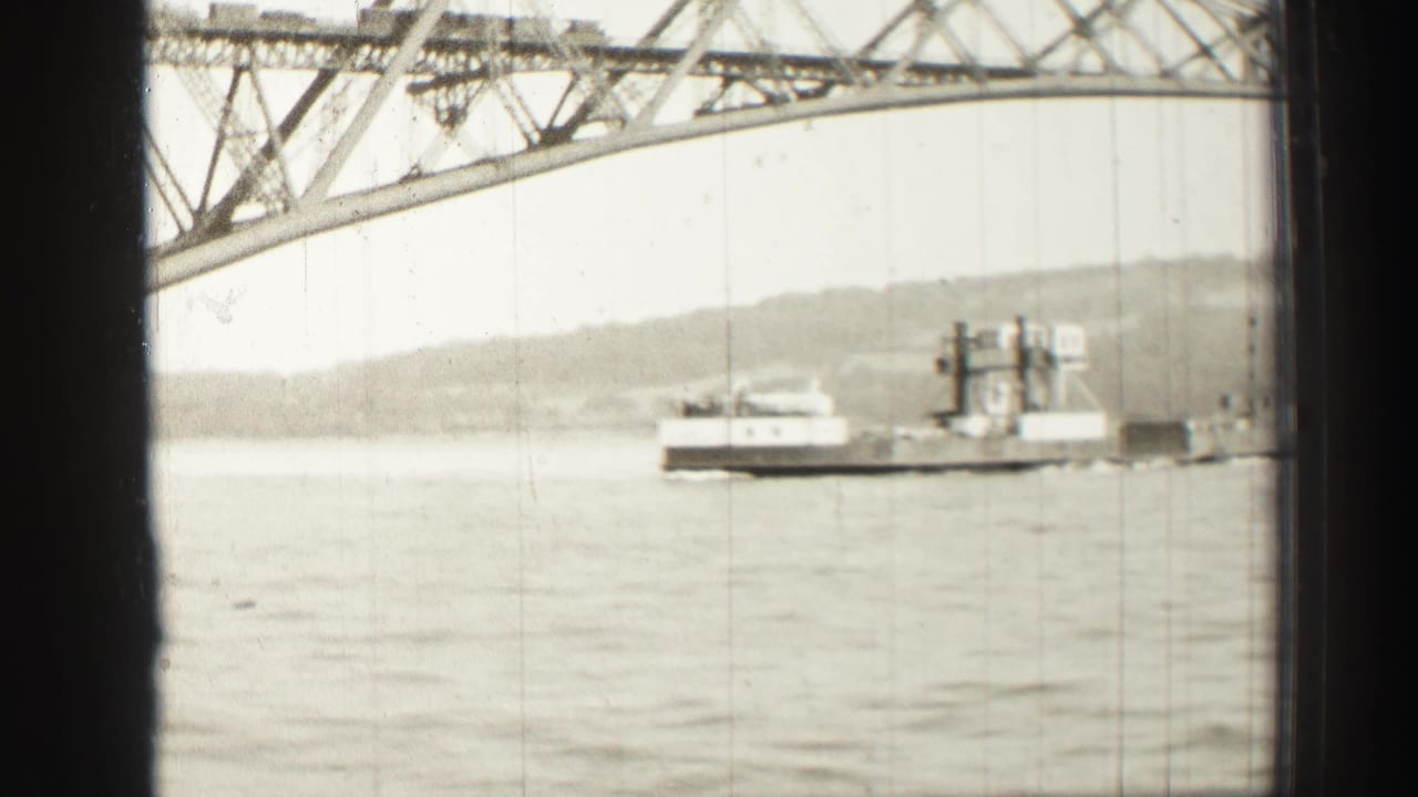 Ferry boat near the right side of the frame under a steel bridge span.