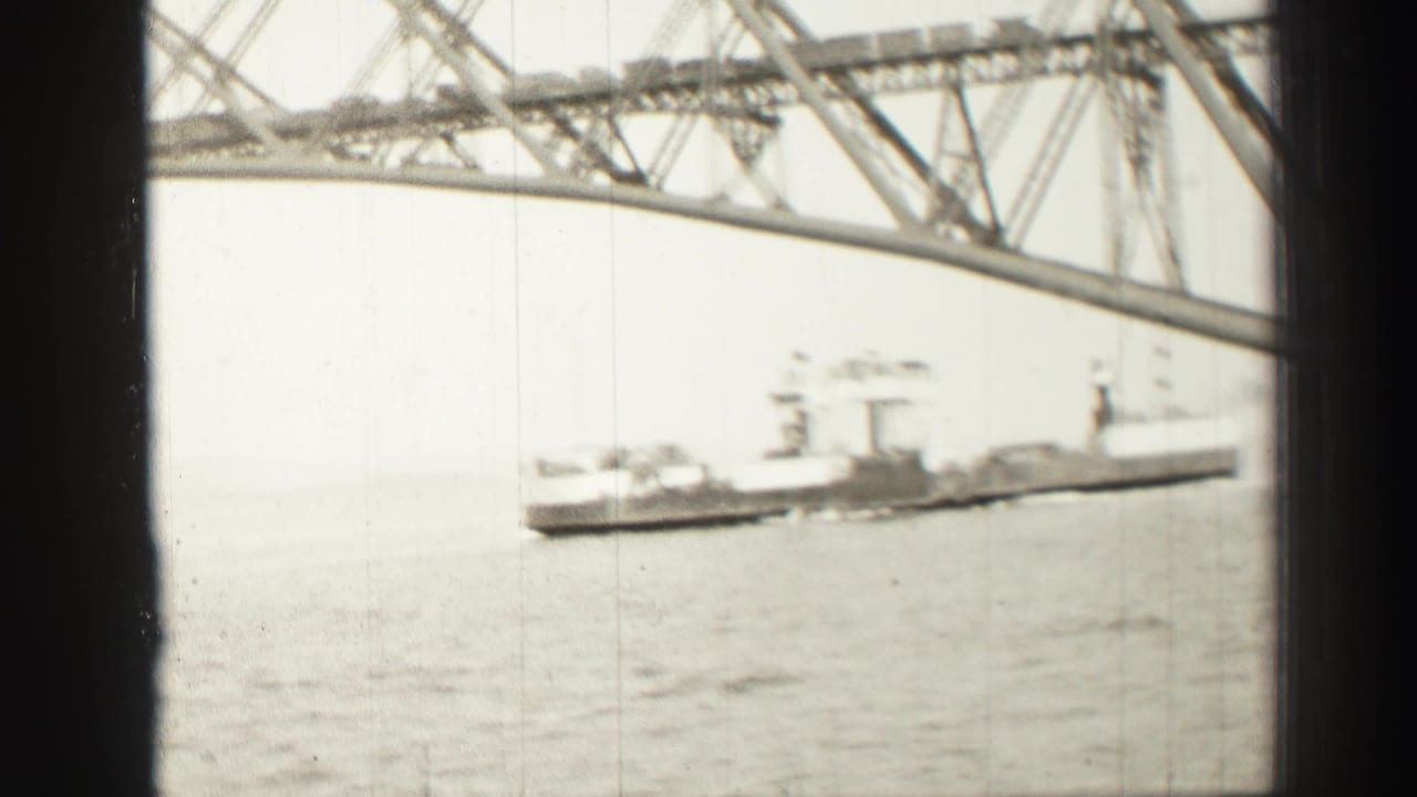 Commercial ship on open water beneath the upper structure of a large steel bridge.