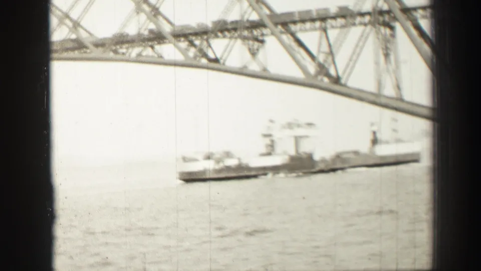 1952 Scotland home-movie frame with a ship moving across water below the high steel truss of a bridge near Edinburgh.