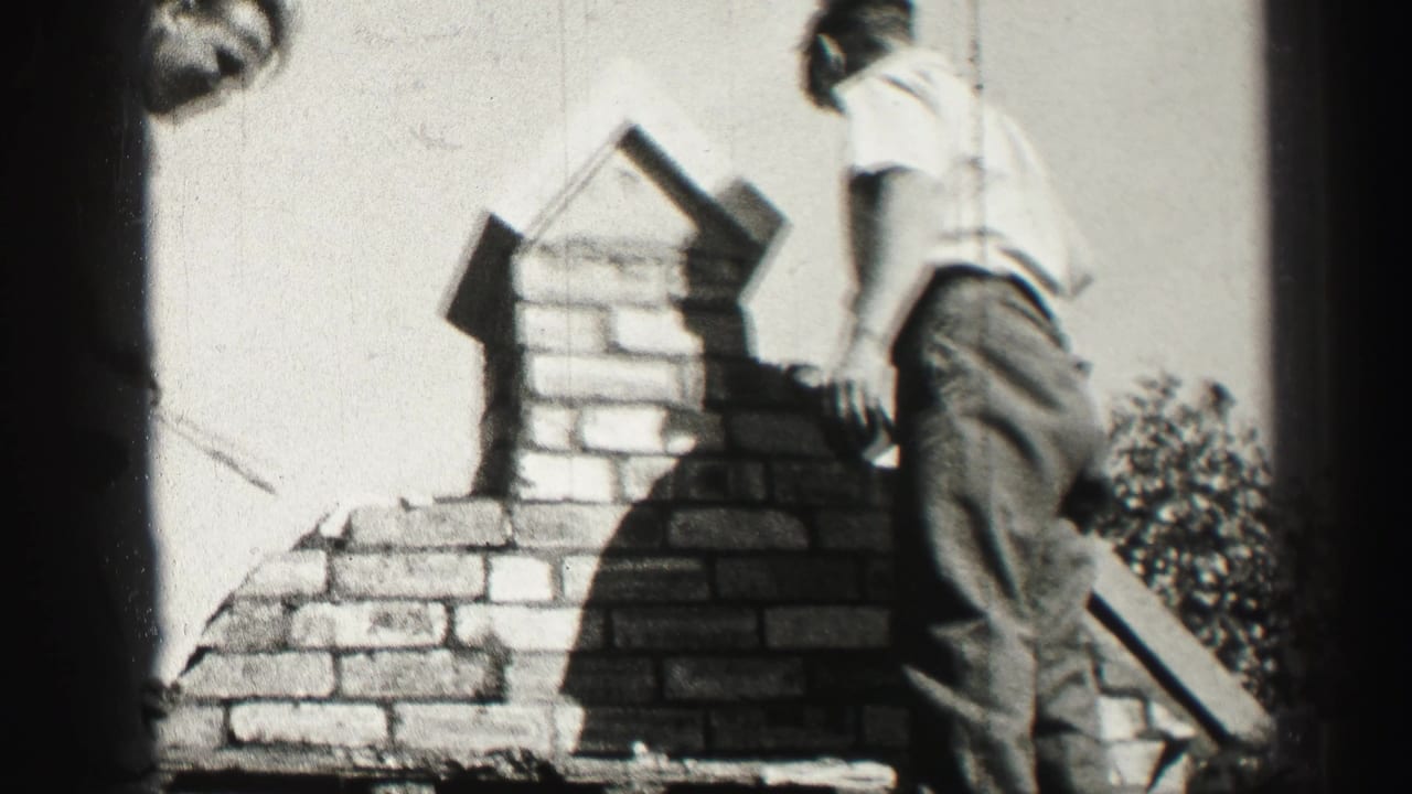 Man standing beside a partly built brick chimney on a roof.