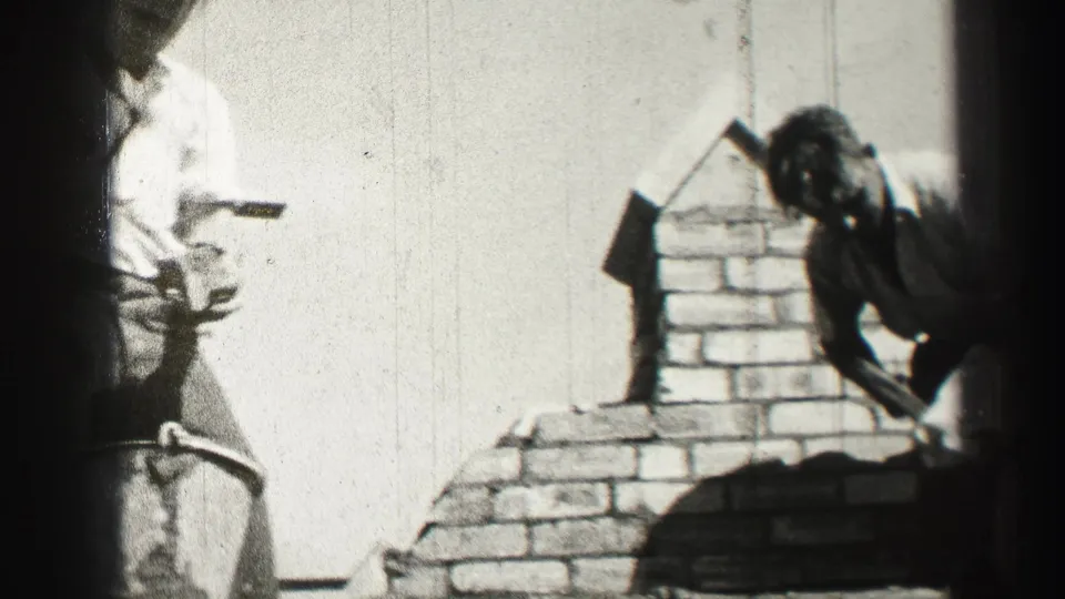 Two men appear partly in frame near the brick chimney, one holding a tool or brick during 1952 rooftop work.