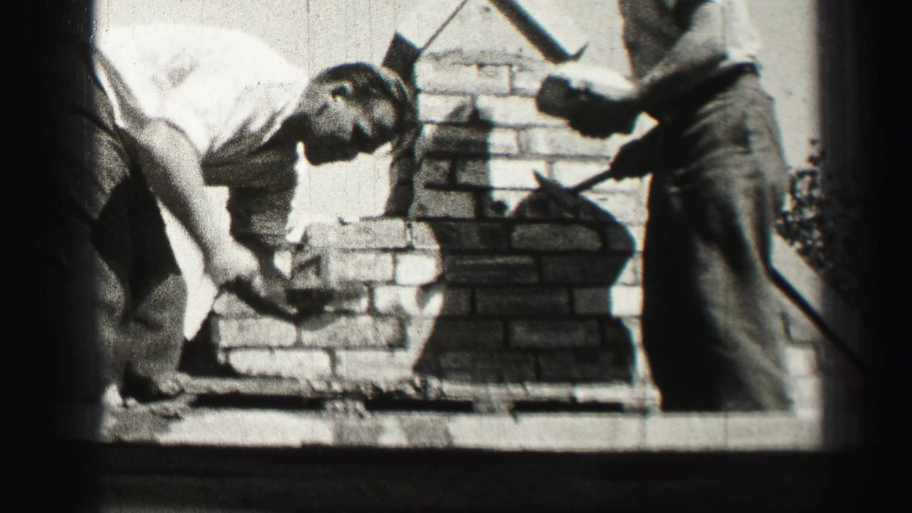 Two adult men work with mortar and bricks on a small masonry structure in 1952 Edinburgh home-movie footage.