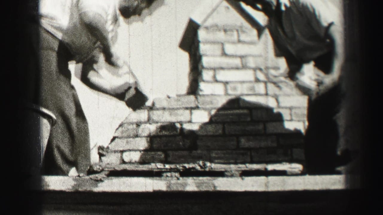 A close home-movie view shows one man applying mortar to brickwork while another worker stands nearby in Edinburgh.