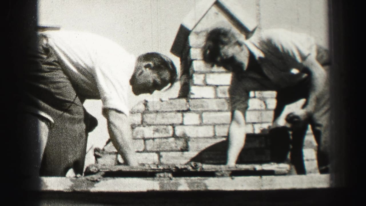 In 1952 Scotland home-movie footage, two adult workers bend over brick courses while building or repairing a chimney with trowels.