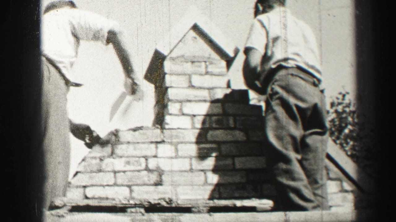 Workers stand beside a partially built brick chimney, one holding a trowel near fresh mortar.